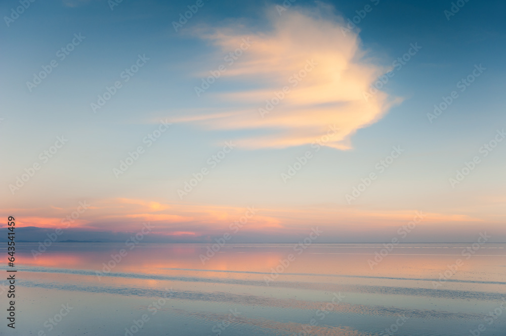 Salar de Uyuni salt flat in Bolivia. Sky with clouds are reflected in the water surface at sunset.