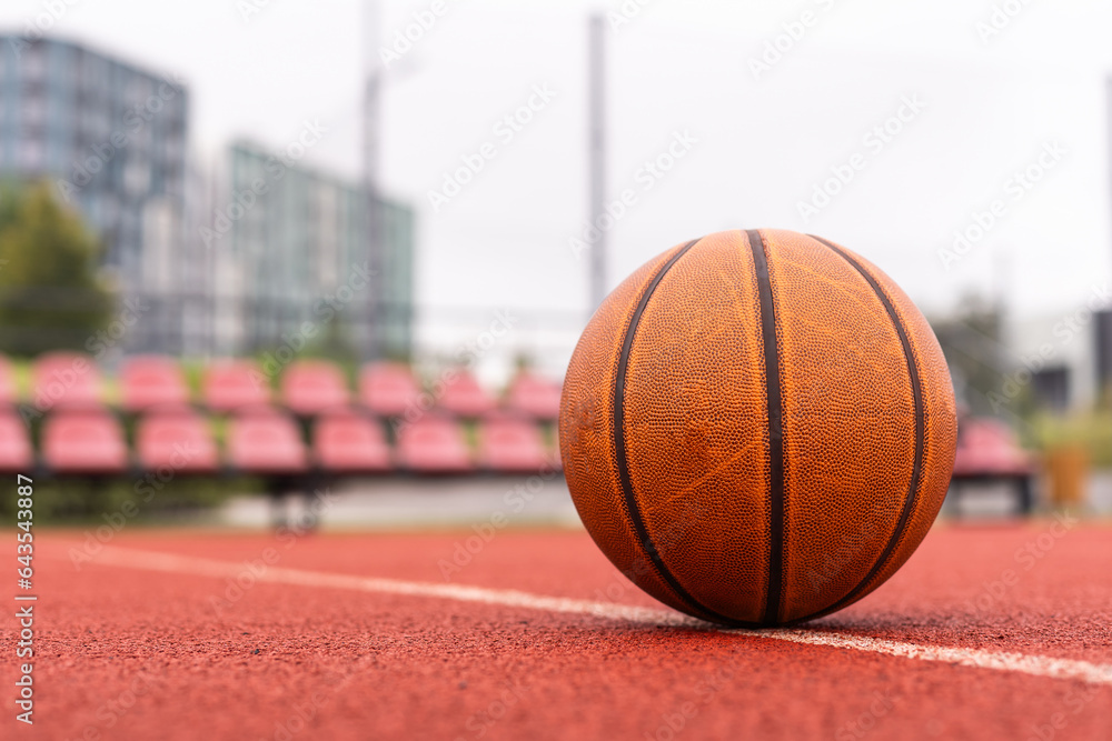 Basketball ball on the ground. Close-up ball on the red court. Basketball on the street or indoor court. Sports gear without people. Minimalism. Template, sport background Basketball ball on the ground. Close-up ball on the red court. Basketball on the street or indoor court. Sports gear without people. Minimalism. Template, sport background