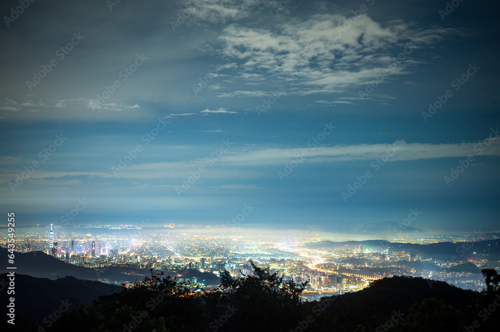 Urban Splendor at Night: Watching Dynamic Clouds Above a Dazzling Cityscape. View of the urban landscape from Dajianshan Mountain, New Taipei City, Taiwan.