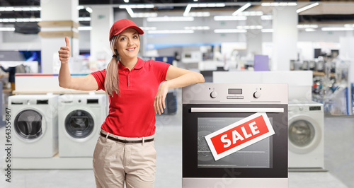 Female shop asisstant standing next to an electrcal oven inside a store photo