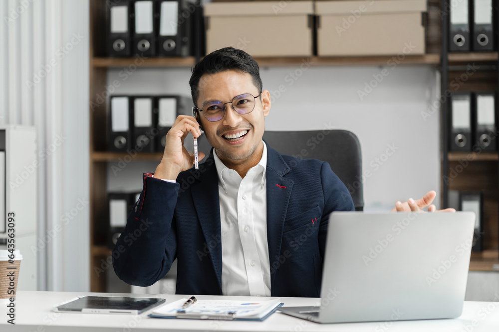 Smiling Asian young freelancer working from home remotely.He is talking on the phone. Smiling Asian young freelancer working from home remotely.He is talking on the phone.