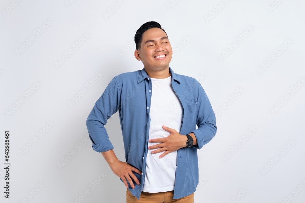 Portrait of young Asian man in casual shirt feeling happy after eating delicious food and rubbing his belly isolated on white background