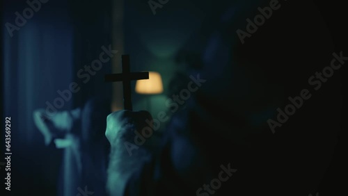 Video of a priest approaching a possessed female, ghost, entity with a knife in hand. The exorcist holds a cross in hand, shaking, scaring the paranormal creature away. photo