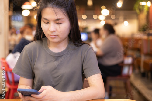 A woman sitting in a restaurant looks at the screen of her cell phone and reads a message with an annoyed expression on her face. Woman waiting for boyfriend who is late. feels loneliness, bad news.