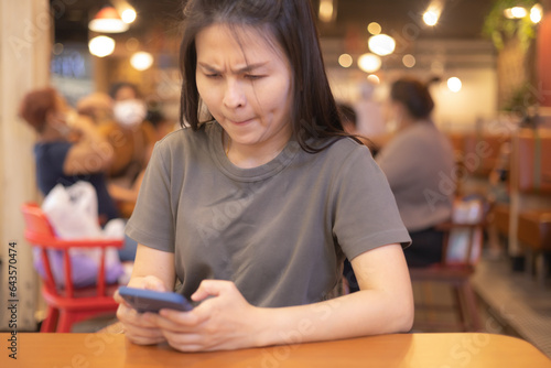 Stressed woman sitting in a restaurant looks at the screen of her cell phone and reads a message with an annoyed expression on her face. Female in troubles. Failure, feels loneliness, bad news concept