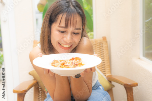 Young Asian woman smiling with her food, spaghetti, A woman holding plate of spaghetti with feeling happy and enjoy to eat food in the restaurant. Enjoy eating concept. Italian food.