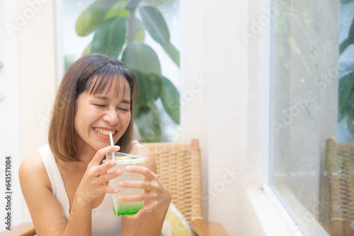 Young Asian woman smiling with apple soda, A woman holding a glass of apple soda with feeling happy and enjoy to eat food in the restaurant. Enjoy eating, refreshing summer drinks, Taste concept.