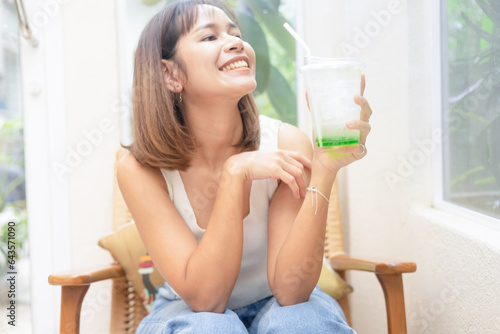Young Asian woman smiling with apple soda, A woman holding a glass of apple soda with feeling happy and enjoy to eat food in the restaurant. Enjoy eating, refreshing summer drinks, Taste concept.