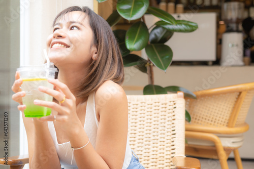 Young Asian woman smiling with apple soda, A woman holding a glass of apple soda with feeling happy and enjoy to eat food in the restaurant. Enjoy eating, refreshing summer drinks, Taste concept.