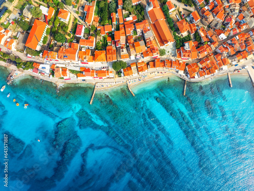 Fototapeta Naklejka Na Ścianę i Meble -  Aerial view of buildings with orange roofs, beach, clear blue sea in summer day. Vacation in beautiful Baska city, Krk island, Croatia. Top drone view of houses, streets, promenade, adriatic sea bay