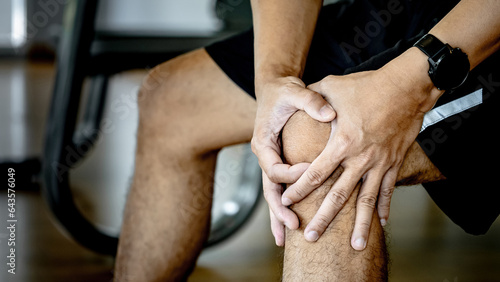Obraz na plátne Sportive man feeling knee pain or rheumatoid arthritis while sitting on workout bench in fitness gym
