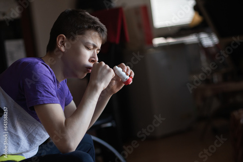 A teenage boy uses an allergy and asthma inhaler photo