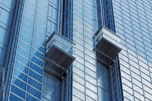 Two external elevators going up along a tall skyscraper. Reflective glass facade