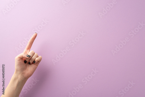 From first person top view, the hand of a young lady, complete with stylish black manicure, creates a pointed gesture using her index finger. The lilac background provides text or ad placement photo