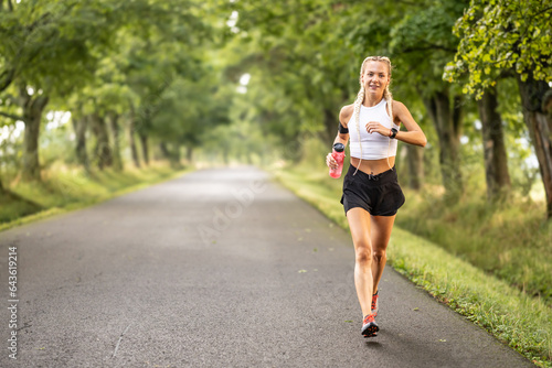 Female runner jogging outside in the park. Young woman runner running with a bottle of water