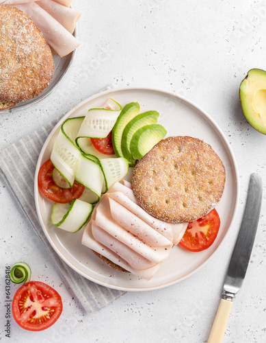 Open sandwich with turkey or chicken ham, sliced cucumber, avocado pieces and fresh tomatoes on white ceramic plate. Top view table. Healthy eating concept. Copy space. Vegetable and oat bread lunch.