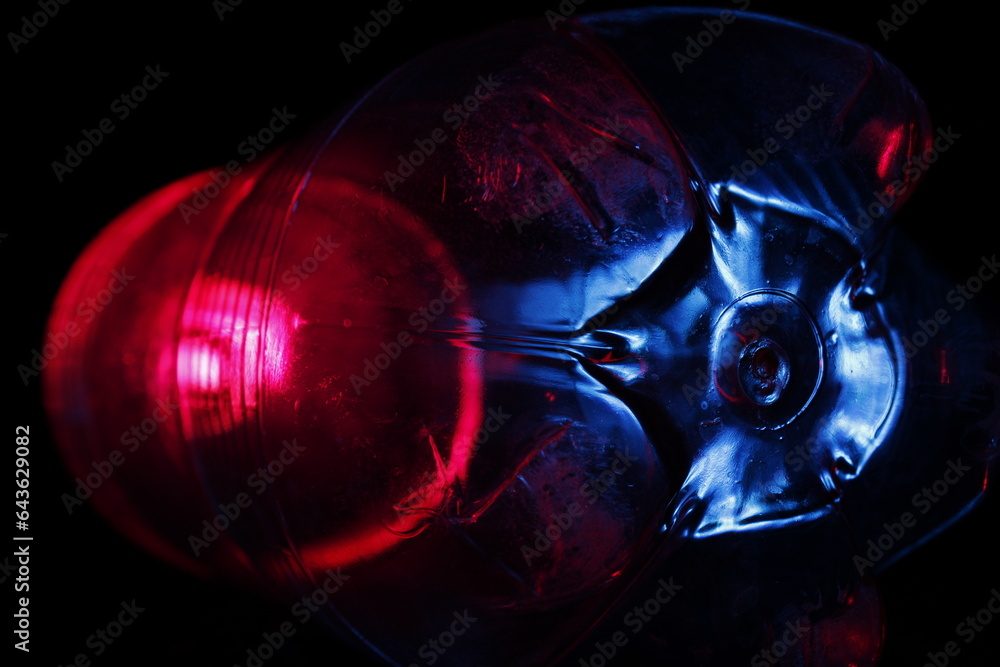 La base de una botella de refresco de plástico retroiluminada muestra una base hexagonal con una esfera roja, formando un original y bonito diseño abstracto sobre un fondo negro.