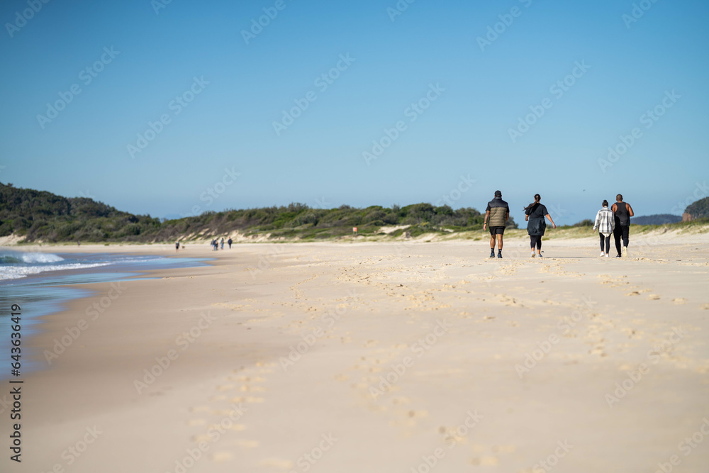 walking on Sandy beach, next to the sea with waves breaking behind, and mountains in the distance