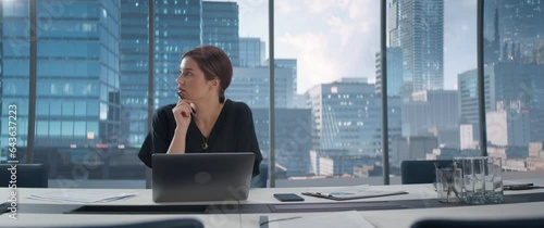 Portrait of Successful Young Businesswoman Sitting at Her Desk Working on Laptop Computer in Big City Office. Professional Social Media Strategy Manager Plan e-Commerce Campaign. Anamorphic Shot photo