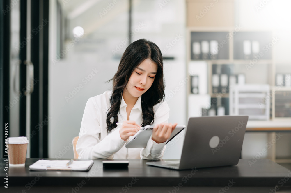 Successful Asian Businesswoman Analyzing Finance on Tablet and Laptop at Office Desk tax, report, accounting, statistics, and analytical research concept. Successful Asian Businesswoman Analyzing Finance on Tablet and Laptop at Office Desk tax, report, accounting, statistics, and analytical research concept.