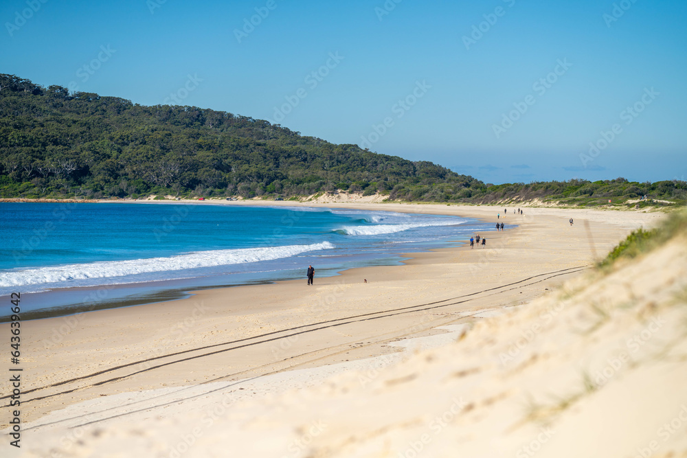 walking on Sandy beach, next to the sea with waves breaking behind, and mountains in the distance