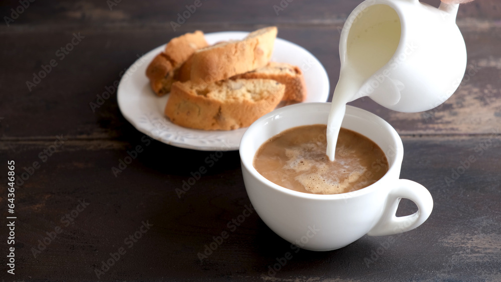 Adding milk cream into black coffee. Coffee with milk and italian cookies Cantucci. Wooden table background Adding milk cream into black coffee. Coffee with milk and italian cookies Cantucci. Wooden table background