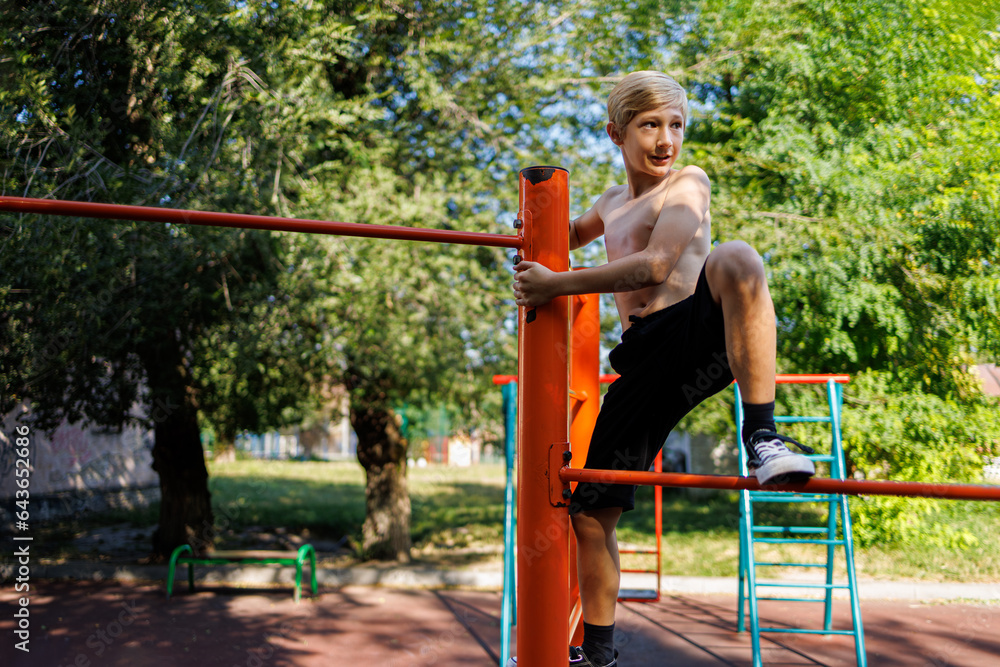 Fototapeta premium A boy in a school park climbed to the top rung Street workout on a horizontal bar in the school park.