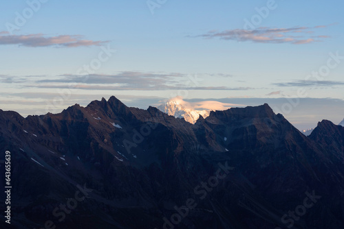 View of Mont Blanc from Gran Paradiso National Park glacier at sunrise. orange yellow colored peak in the background, foreground mountains and valley in the shadow