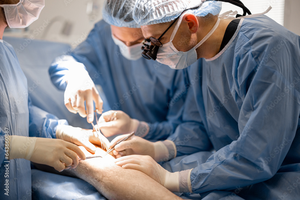 Three confident surgeons performing surgical operation on a patient's knee in operating room. Concept of real surgery and invasive treatments