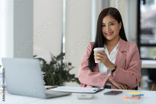 Confident Asian businesswoman working for a real estate project Financial business, accounting and drinking coffee while working, sitting and relaxing, taking a break at the desk.