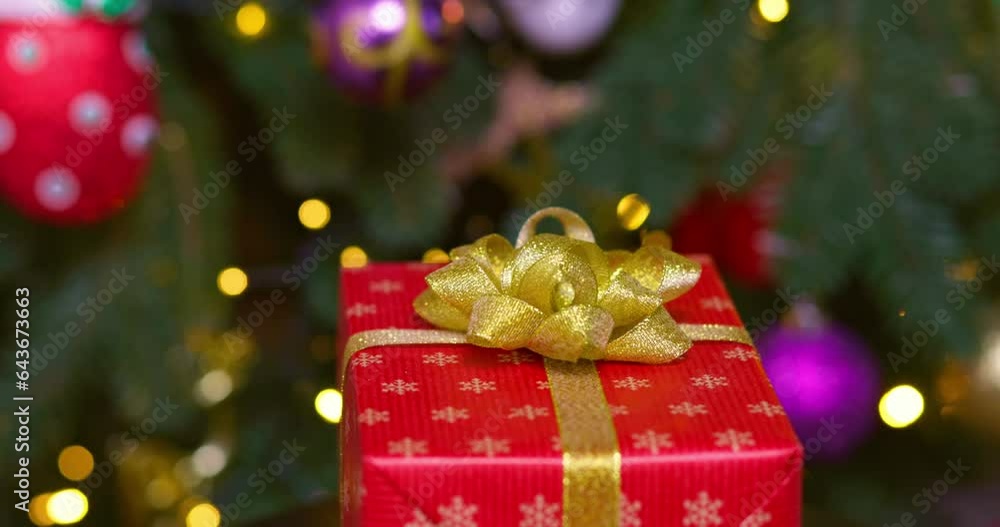 A red box with golden ribbon rotates against background of Christmas tree A red box with golden ribbon rotates against background of Christmas tree