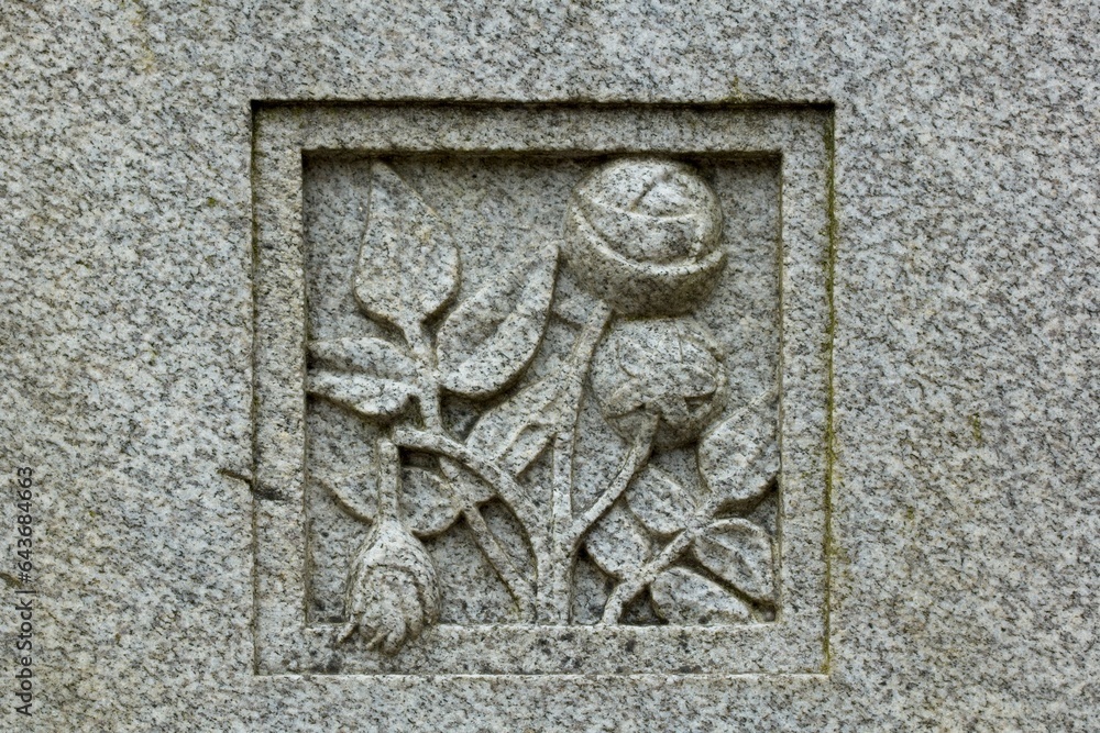 Stone carving of flowers on grave stone in cemetery.