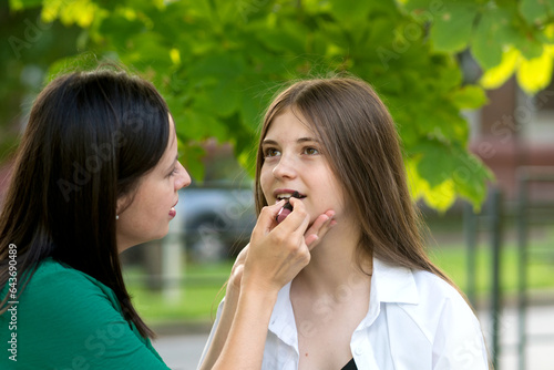 Mom applying lipstick to teenage daughter's lips © Vagengeim