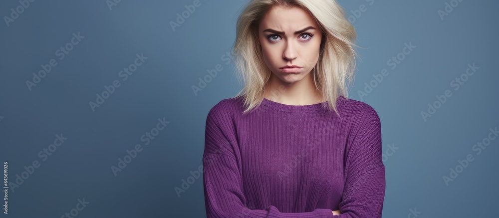 Unhappy attractive blonde woman in purple sweater with disapproval on blue backdrop having room for text