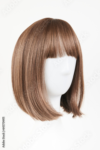Natural looking dark brunet wig on white mannequin head. Middle length brown hair on the plastic wig holder isolated on white background, side view.