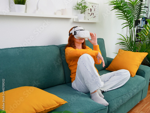 Obraz na płótnie woman sitting on sofa relaxing and playing VR and using futuristic artificial intelligence at home.. the concept of metaverse, virtual reality, future, technology, and internet of things. w salonie
