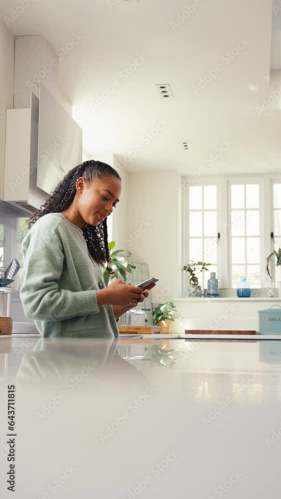 Vertical video of teenage girl at home in kitchen connecting with her friends using social media and text messaging - shot in slow motion Vertical video of teenage girl at home in kitchen connecting with her friends using social media and text messaging - shot in slow motion