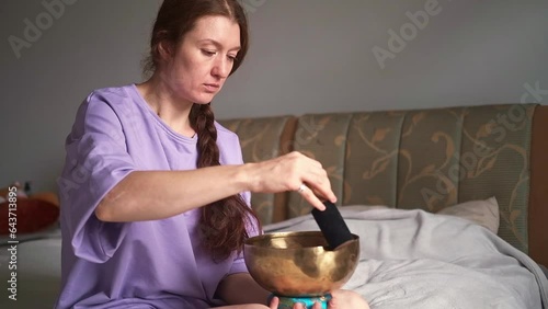 A woman with red hair is sitting at home on the bed and doing meditation with a singing bowl. 