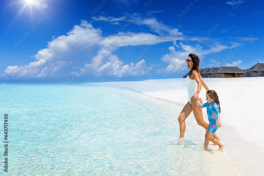 A happy mother and daughter run into the turquoise sea of a tropical paradise beach
