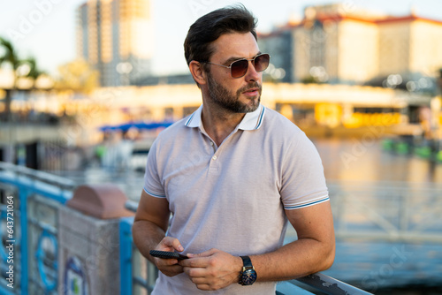 Casual handsome man chatting on phone in urban city. Well-dressed man talking on phone outdoor. Businessman using phone. Phone conversation in city. Outdoor fashion portrait.