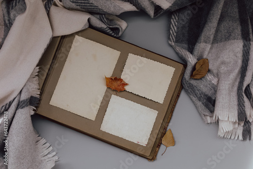 Clear blank photo frames on old album with grey plaid and fall leaves. Sunday loneliness relaxing, hugge mood. Family traditions, memories and nostalgia concept. Flat lay. Autumn vibes
