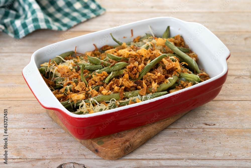 A traditional green bean casserole topped with French Fried Onions and cream of mushroom on wooden table A traditional green bean casserole topped with French Fried Onions and cream of mushroom on wooden table