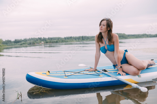 Sticker A young woman with an open swimsuit swims on a SUP board on a picturesque lake