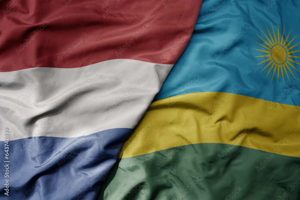 big waving national colorful flag of netherlands and national flag of rwanda .