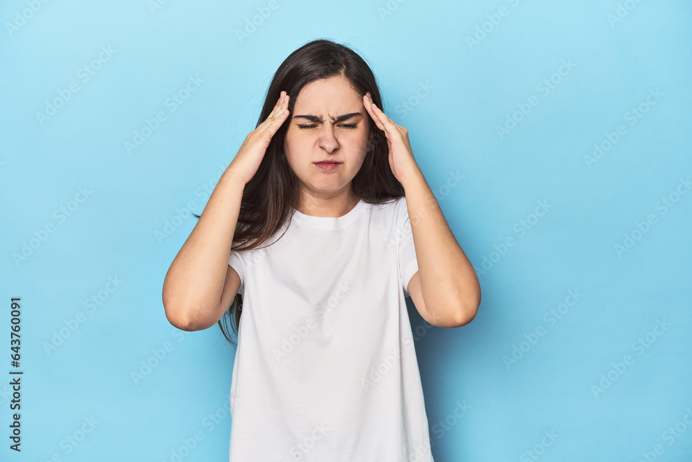Young Caucasian woman on blue backdrop touching temples and having headache. Young Caucasian woman on blue backdrop touching temples and having headache.