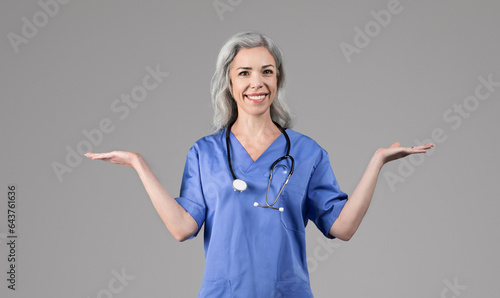 Cheerful nurse lady holding hands comparing something over gray background