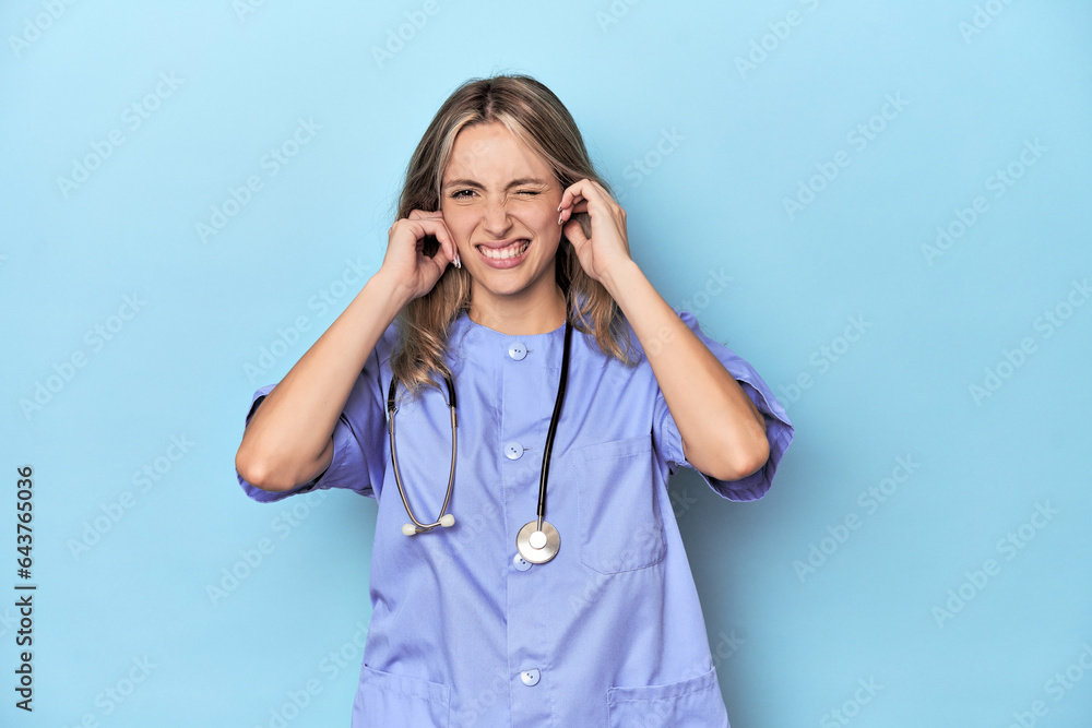 Young caucasian nurse in blue studio covering ears with hands. Young caucasian nurse in blue studio covering ears with hands.