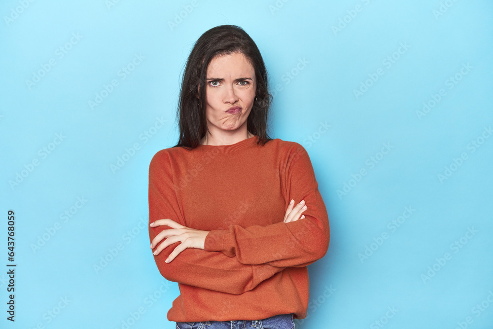 Young caucasian woman on blue backdrop frowning face in displeasure, keeps arms folded. Young caucasian woman on blue backdrop frowning face in displeasure, keeps arms folded.