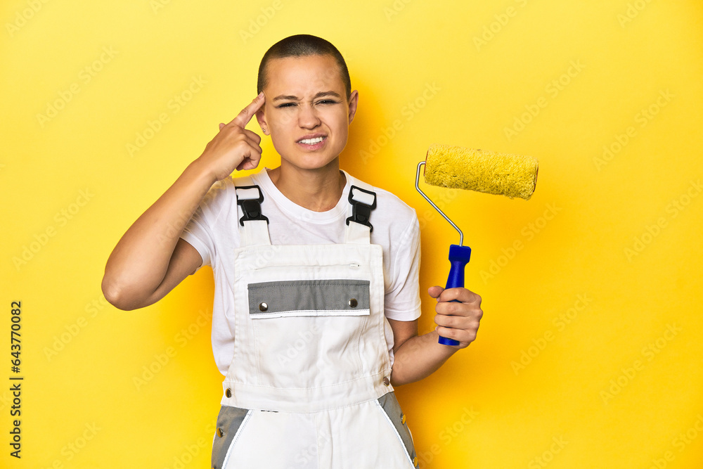 Painter woman, shaved head, with yellow roller in studio showing a disappointment gesture with forefinger. Painter woman, shaved head, with yellow roller in studio showing a disappointment gesture with forefinger.