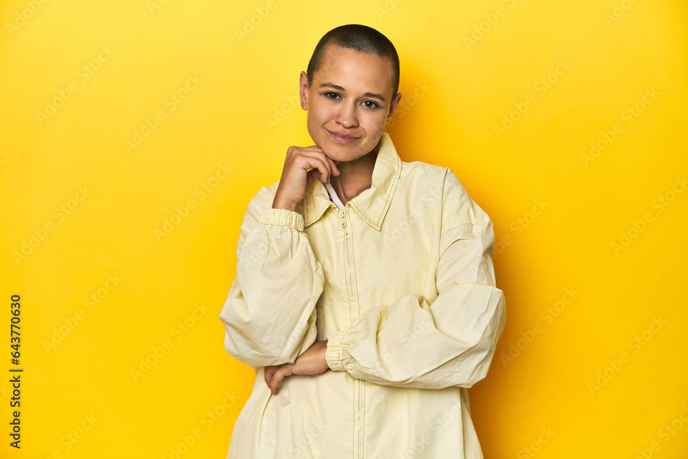Young woman in jacket, yellow studio backdrop smiling happy and confident, touching chin with hand. Young woman in jacket, yellow studio backdrop smiling happy and confident, touching chin with hand.